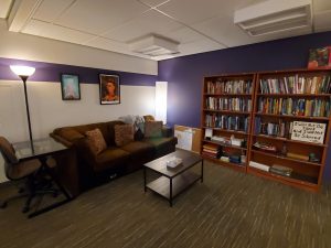 Image shows the D Center space, which is square with bookshelves along the back wall. A brown couch and a coffee table sit in front of it. 
