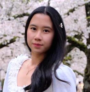 Feminine looking person with white top and a white floral background, looking intently forward.